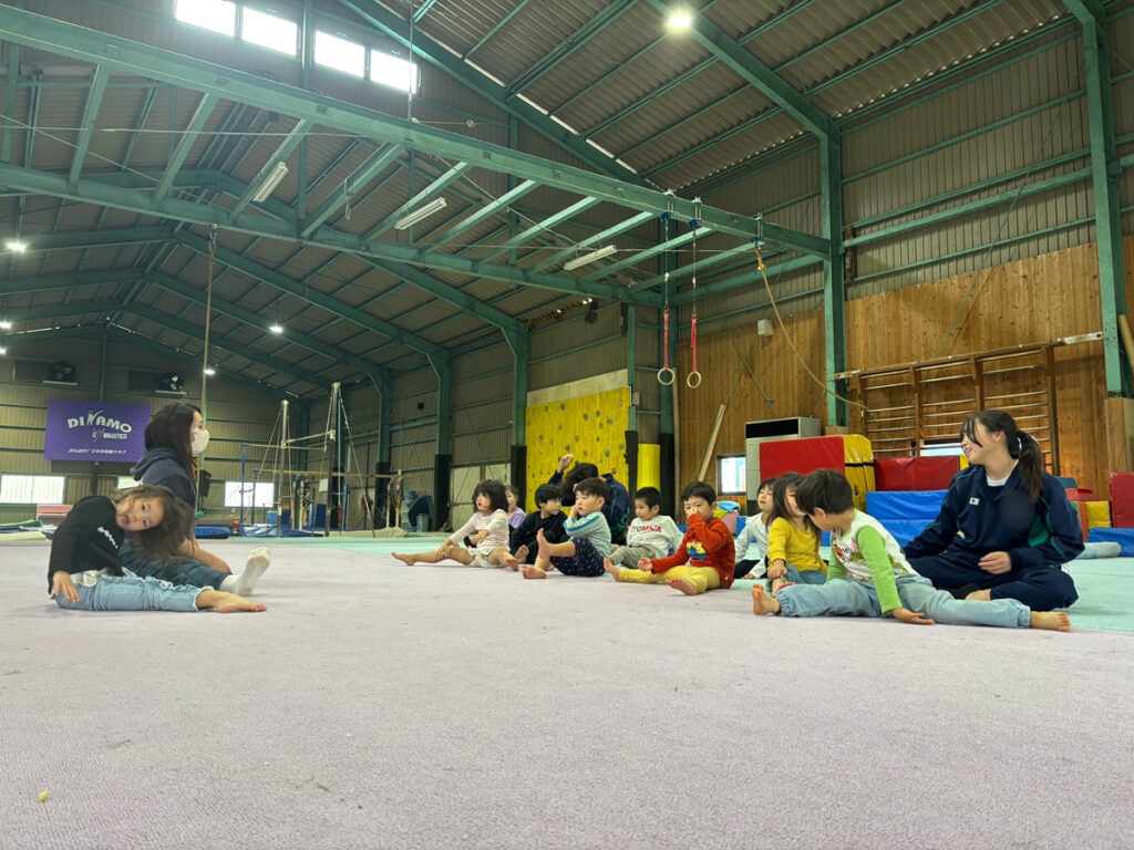 ディナモ体操クラブの広い体育館で座学や準備運動に取り組むタイムカプセル保育園の園児とインターンシップ生