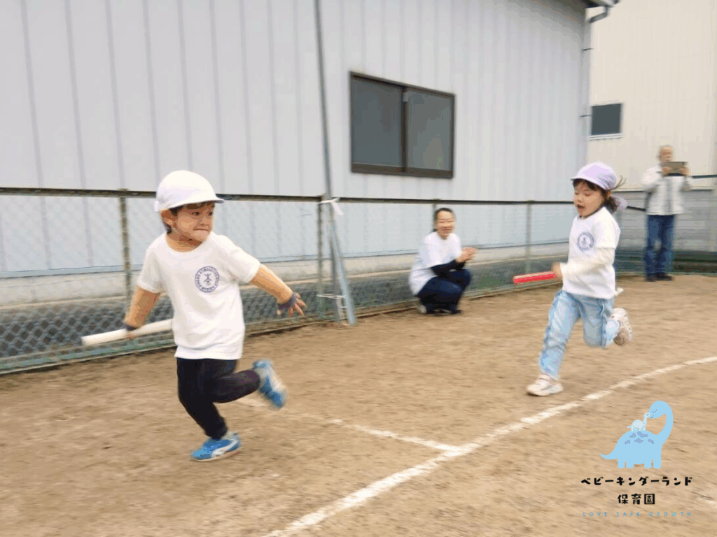 タイムカプセル保育園の運動会でのリレー競技。白い帽子とユニフォームを着た男の子と女の子がバトンを持ってグラウンドを走っている様子。