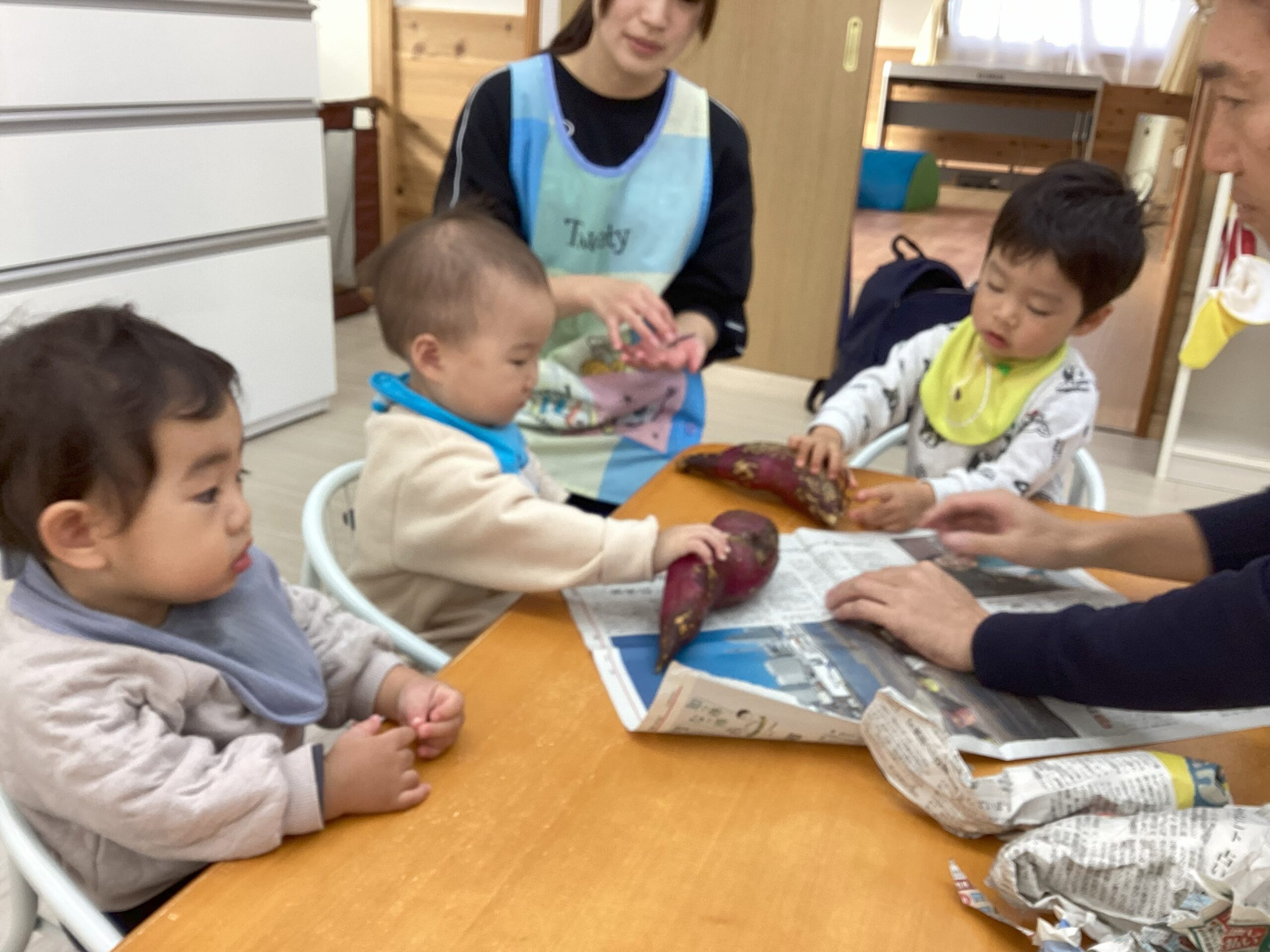 タイムカプセル保育園の焼き芋大会準備。大きなサツマイモを不思議そうに見つめ、一生懸命に手を伸ばして感触を確かめる子どもたち