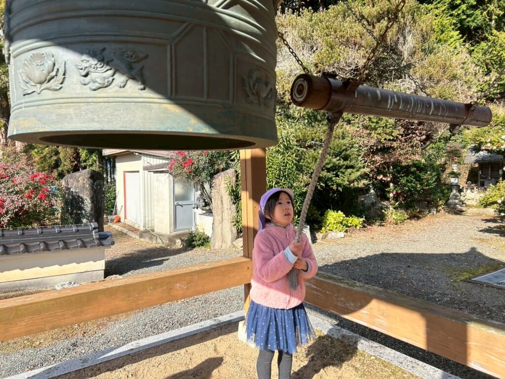 お寺の鐘を鳴らして、その音色と大きさに驚きと感動の表情を見せる女の子。