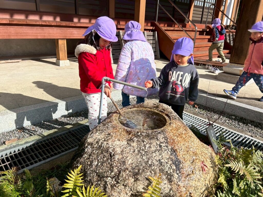 お寺の手水舎で、柄杓を使って手を清める体験をするタイムカプセル保育園の子どもたち。