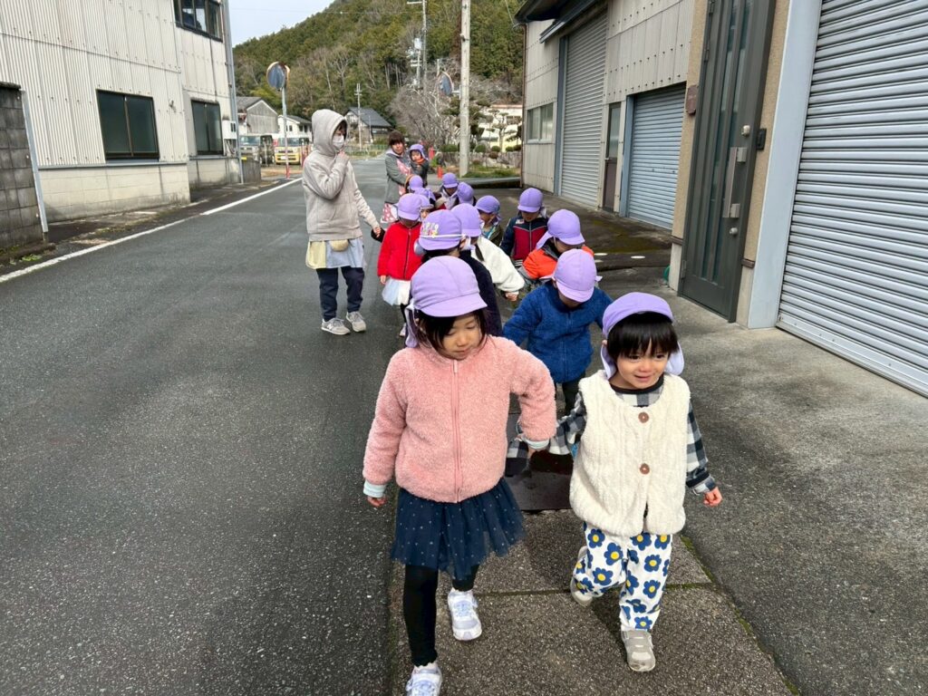 氷上町ののどかな道を、お友だちと手をつないで元気にお散歩するタイムカプセル保育園の子どもたちと保育士。