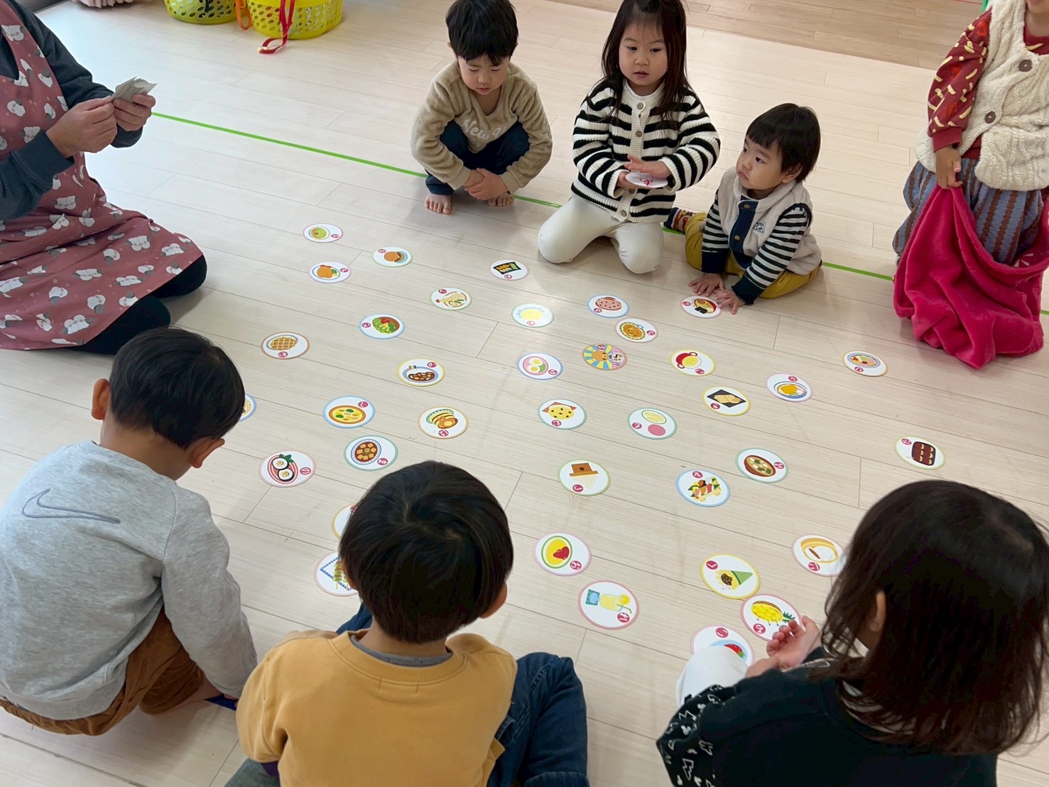 タイムカプセル保育園の室内で、保育士と子どもたちがアットホームな雰囲気で絵カルタ遊びを楽しんでいる様子