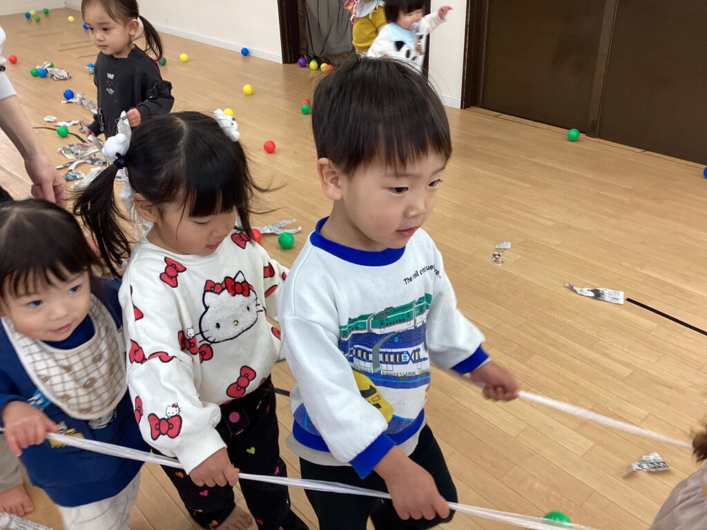 タイムカプセル保育園の室内で、お友達と紐を持って一列に並び、元気いっぱい「電車ごっこ」を楽しむ子どもたち