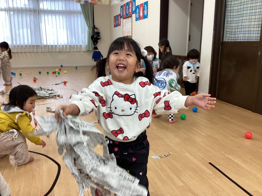 タイムカプセル保育園の室内で新聞紙を片手に満面の笑顔で走る女の子