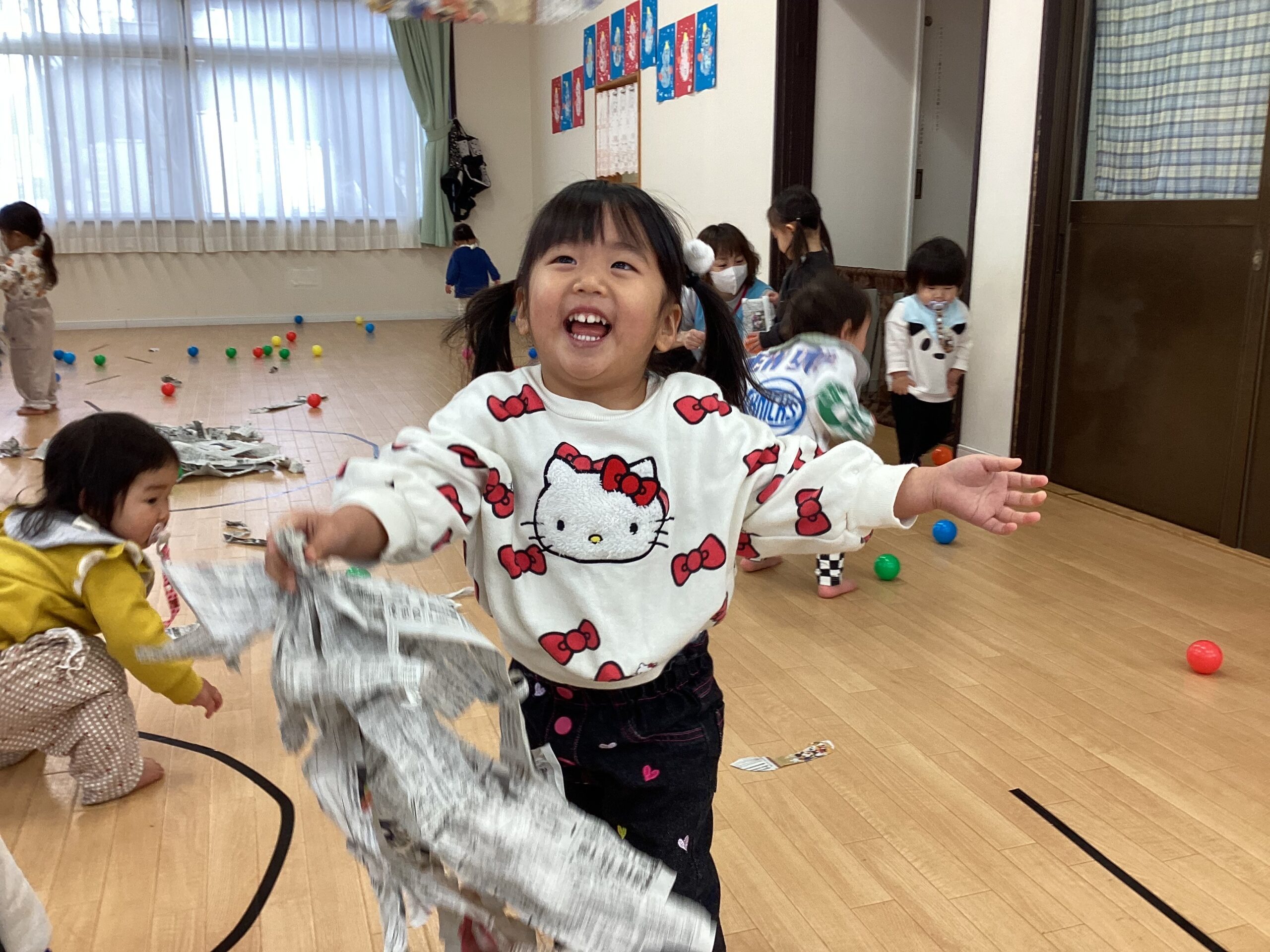タイムカプセル保育園の室内で新聞紙を片手に満面の笑顔で走る女の子