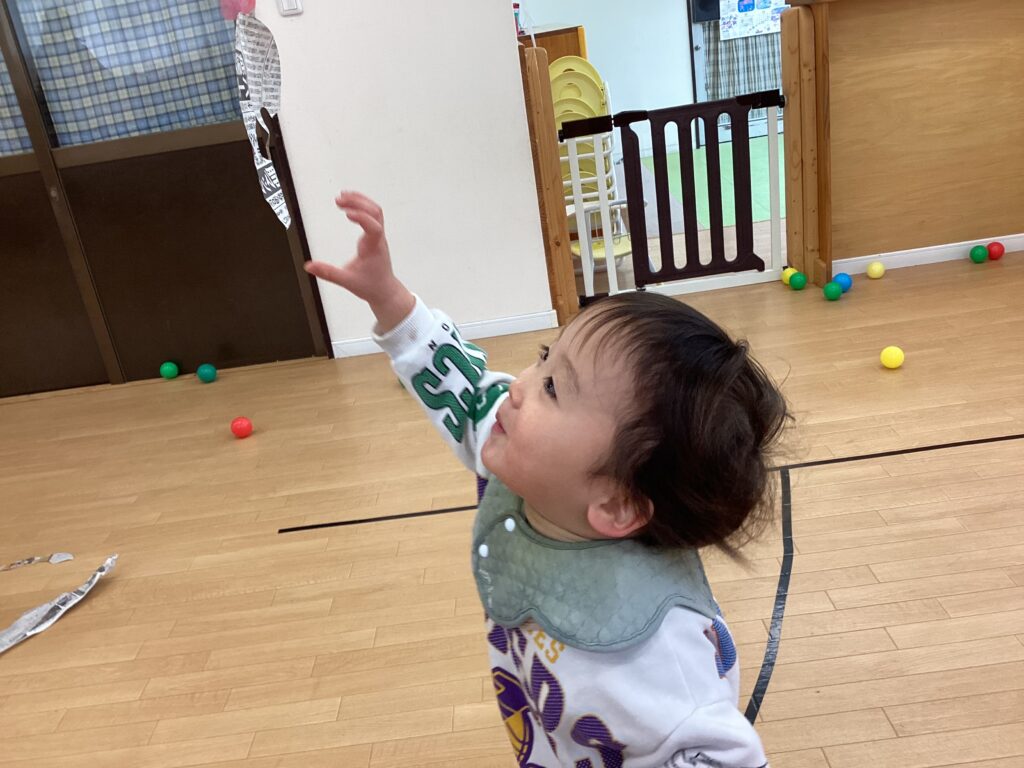 タイムカプセル保育園の室内遊びで、宙を舞う新聞紙に興味津々で手を伸ばす小さな子どもの様子