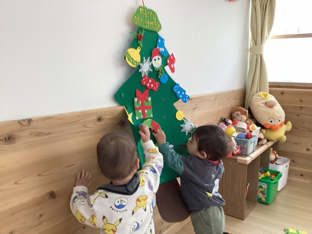 兵庫県丹波市の小規模認可保育園で、クリスマス会に向けてフェルトの壁掛けツリーに飾り付けを楽しむ1歳児クラスの子どもたち