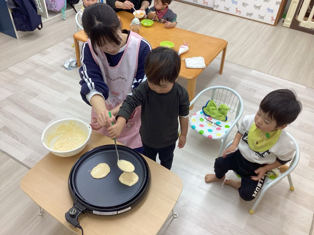 兵庫県丹波市氷上の小規模認可保育園での食育活動。保育士と一緒にホットプレートへ慎重にホットケーキの生地を流し入れる子どもの真剣な表情