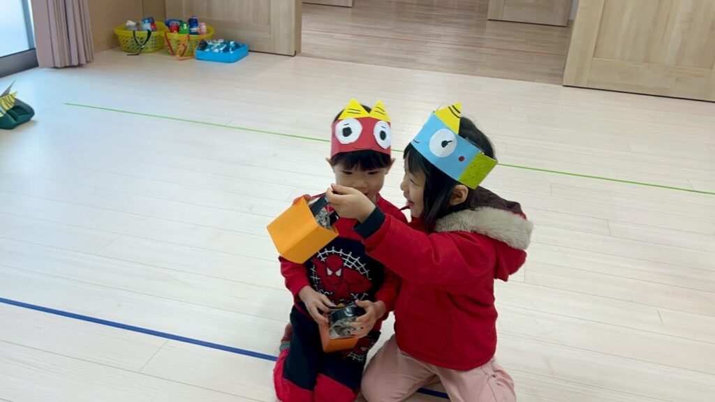 兵庫県丹波市氷上のタイムカプセル保育園の節分会。手作りの鬼のお面をつけた子どもたちが、仲良く寄り添って豆箱を見せ合っている様子