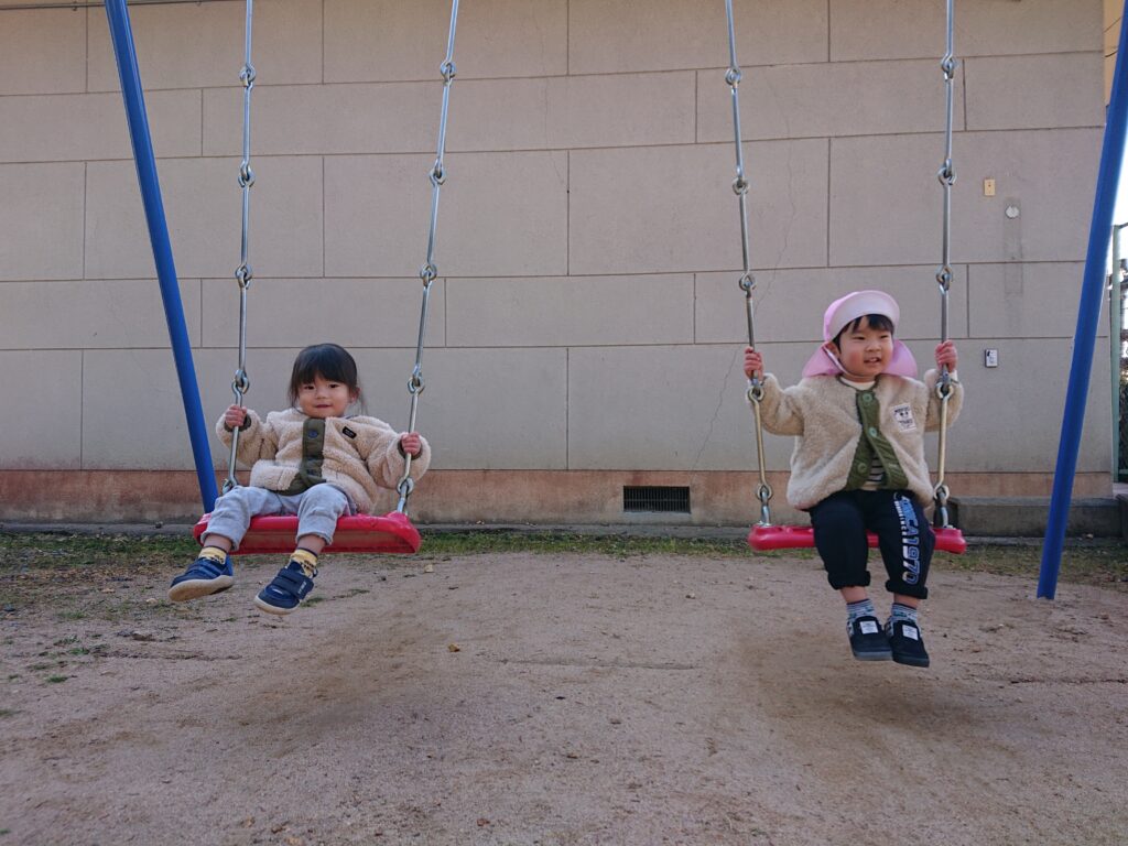 タイムカプセル保育園の公園遊び。ブランコに順番に座って、しっかりとチェーンを握りながら安全に遊ぶ1・2歳児の子どもたち