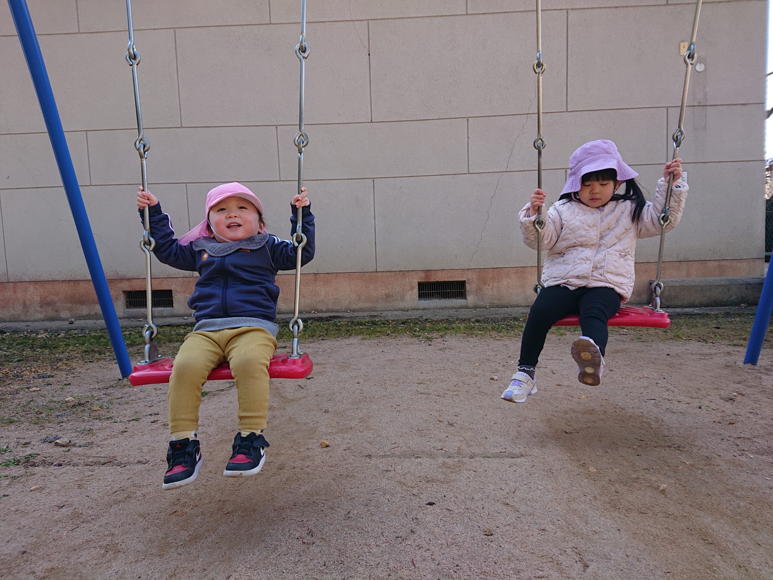 タイムカプセル保育園のお外遊び。公園のブランコに順番に乗って、笑顔でゆらゆらと揺れる1・2歳児クラスの子どもたち