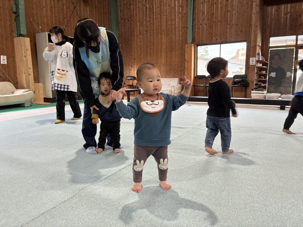 タイムカプセル保育園の体操あそび。体育館の広いマットで、保育士のサポートを受けながらのびのびと体を動かす子どもたち