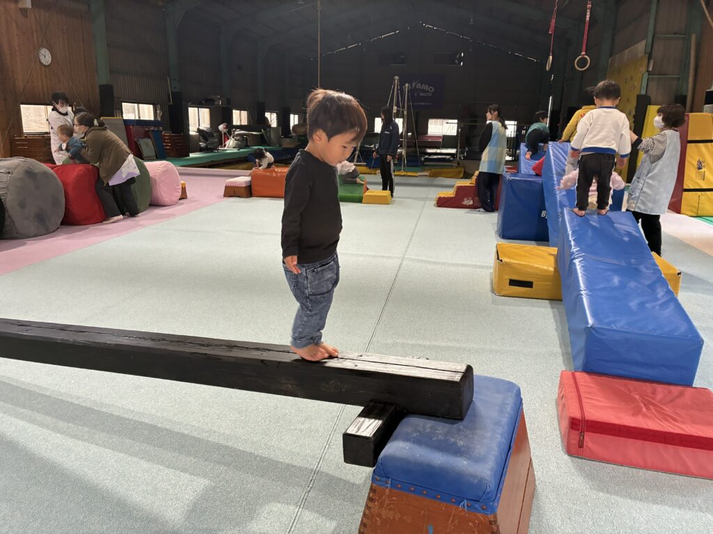 タイムカプセル保育園の体操あそび。体育館に設置された低い平均台を、上手にバランスをとりながら渡る子ども