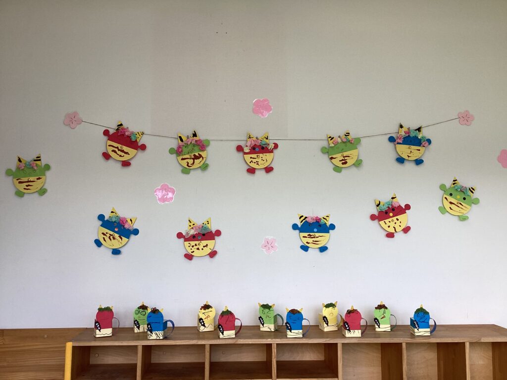 兵庫県丹波市のリトルわんぱく保育園の節分作品展示。壁に飾られたカラフルな鬼の製作と、棚に並んだ牛乳パックの手作り豆箱