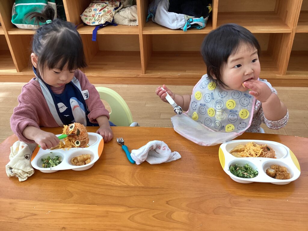 兵庫県丹波市のリトルわんぱく保育園での節分給食。0歳・1歳児クラスの子どもたちが、鬼の顔をした特製オムライスを手づかみやスプーンで食べている様子
