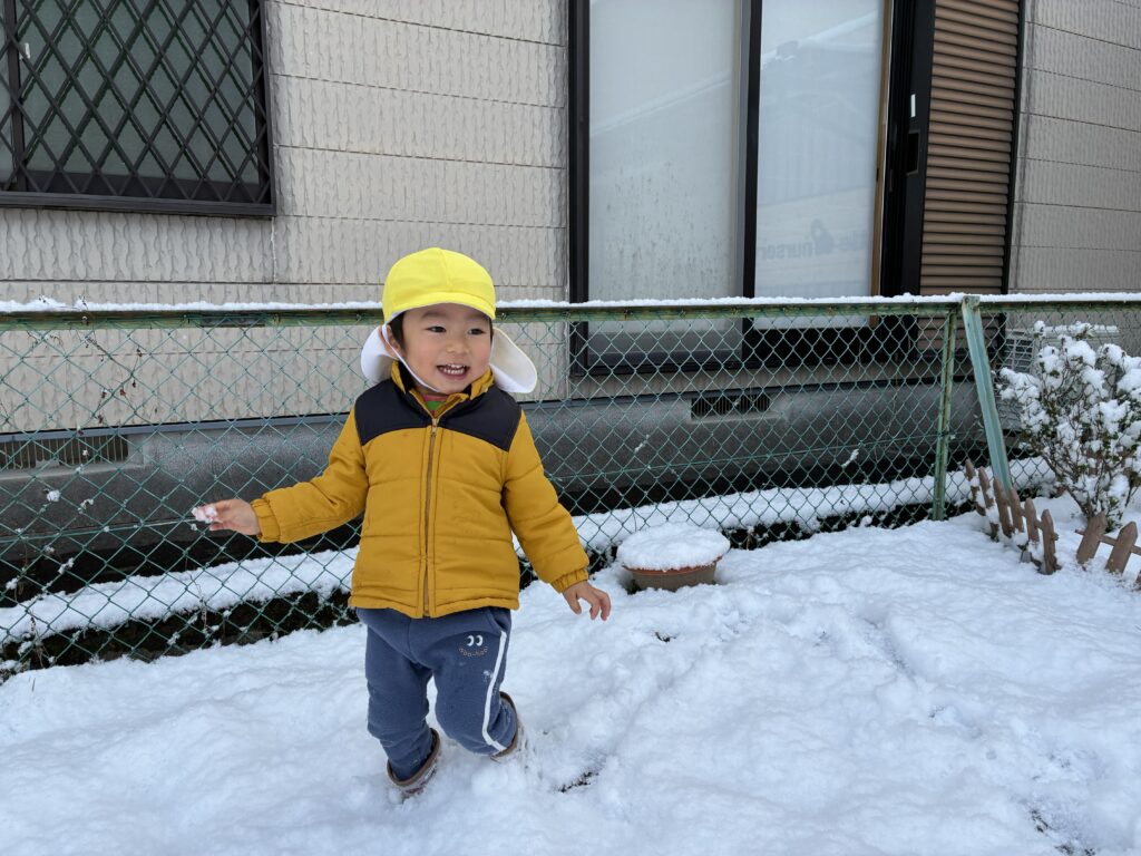 兵庫県丹波市氷上のタイムカプセル保育園での雪遊び。雪が積もった園庭で、黄色い帽子とダウンジャケットを着て笑顔で遊ぶ子どもの様子