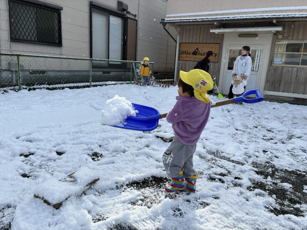兵庫県丹波市氷上のタイムカプセル保育園の園庭で、大きな青いスコップを使って一生懸命雪かきをする子どもの様子