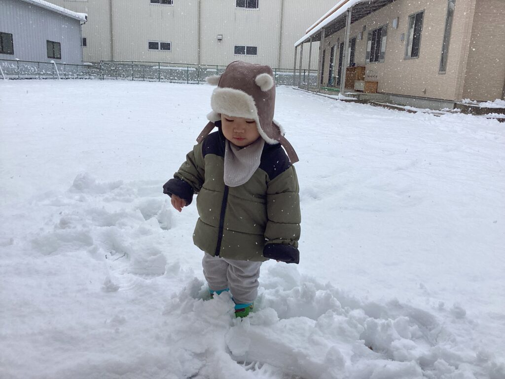 兵庫県丹波市氷上のタイムカプセル保育園の広い園庭で、雪の上を歩く子ども。長靴が雪に埋まる感触や冷たさを足元で確かめている様子