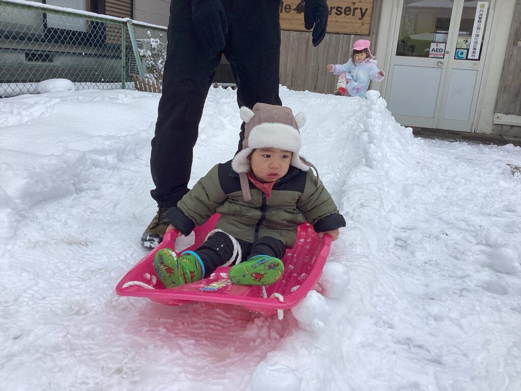 兵庫県丹波市氷上のタイムカプセル保育園でのそり滑り体験。園長先生のサポートのもと、少しドキドキした表情でピンクのそりに乗る子どもの様子