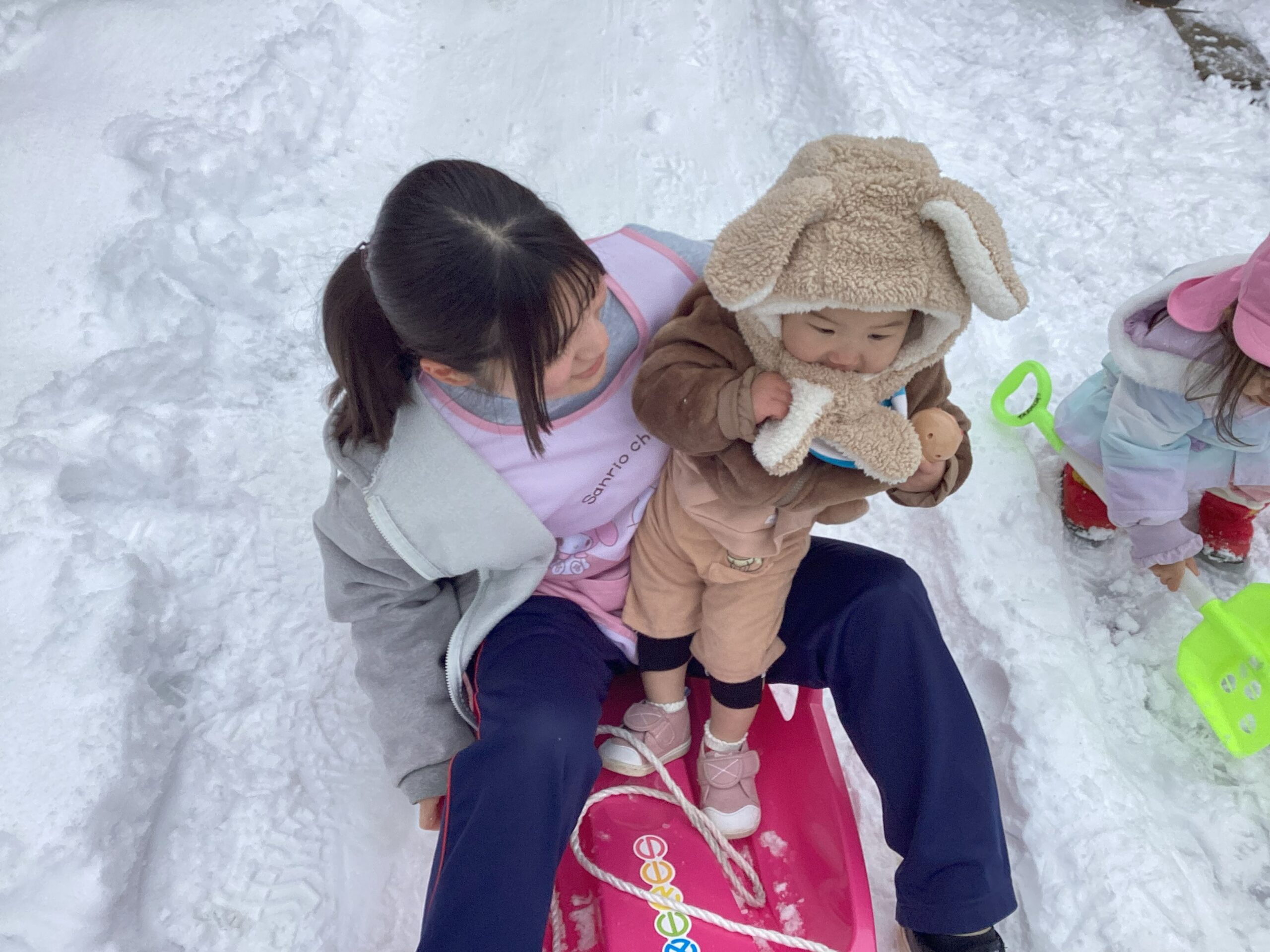 兵庫県丹波市氷上のタイムカプセル保育園での雪遊び。先生と一緒にピンクのそりに乗って、雪の滑り台を滑る子どもの様子